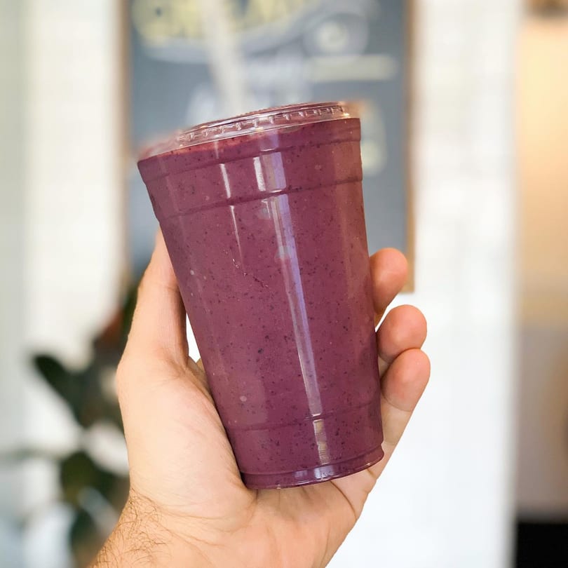 A hand holding a clear plastic cup filled with a vibrant purple smoothie from Juice Parlor NoHo.