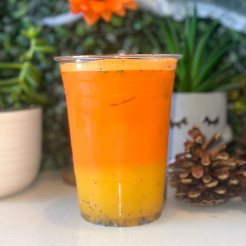 A vibrant orange and yellow layered juice with chia seeds, in a clear cup, on a white counter.