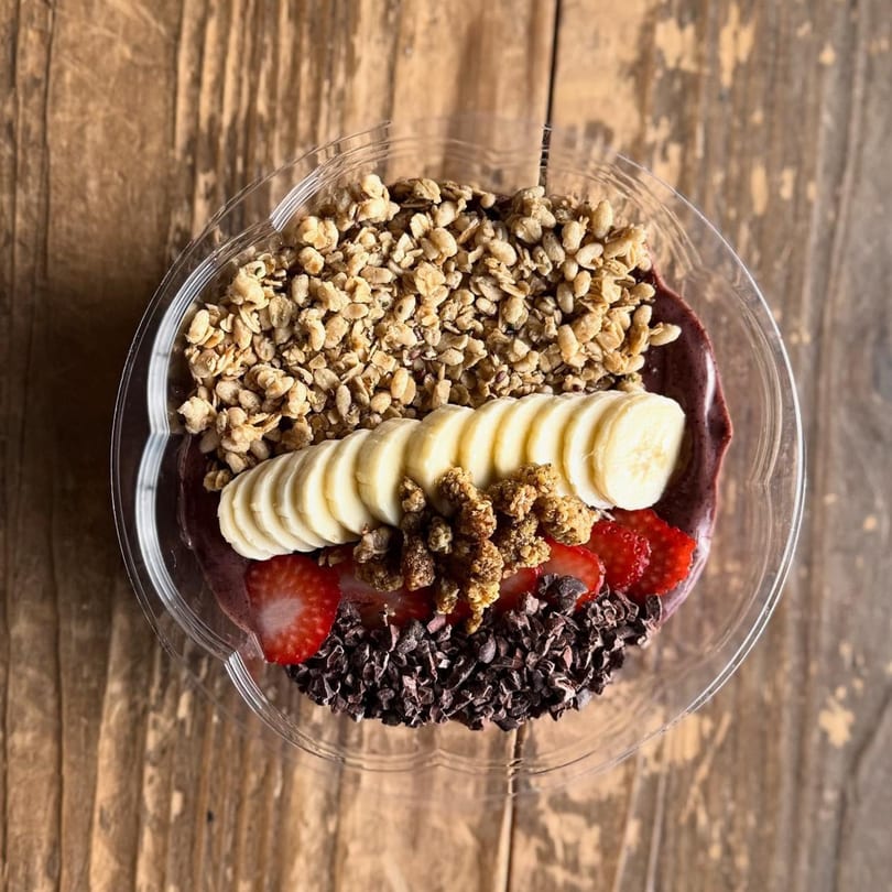 Overhead view of an acai bowl with granola, banana slices, strawberries, and cacao nibs.