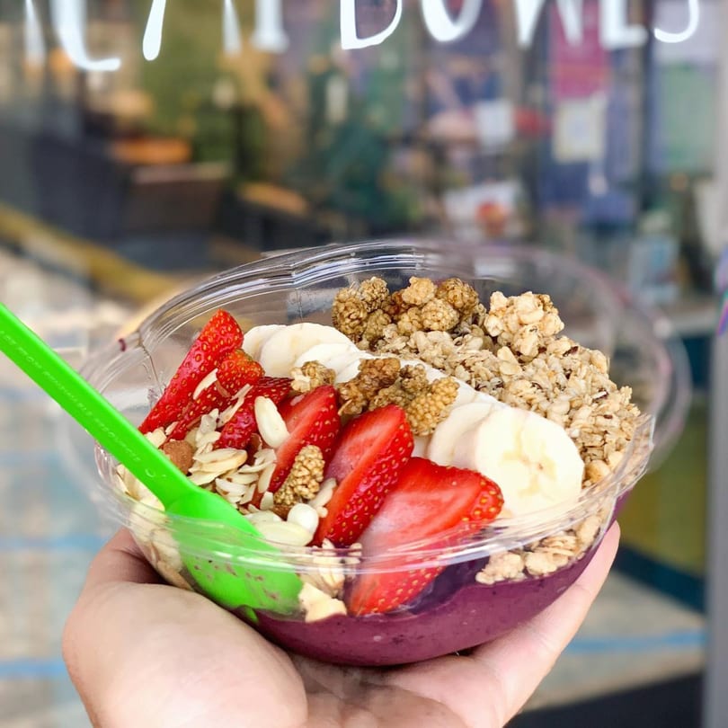 Hand holding a Juice Parlor NoHo acai bowl with strawberries, bananas, granola, and mulberries.