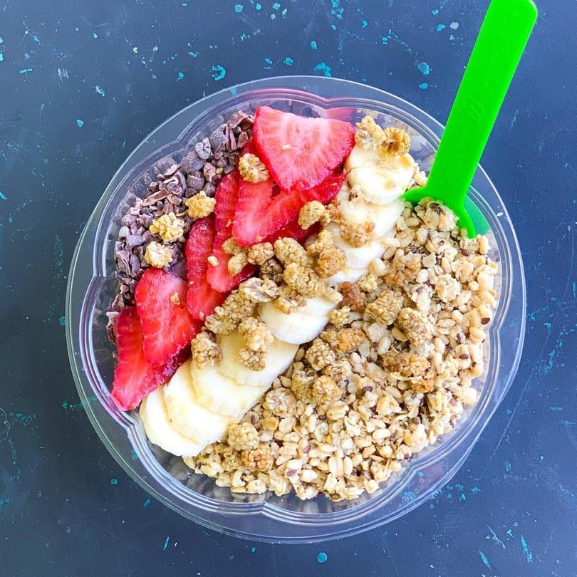 Overhead view of an acai bowl with strawberries, bananas, granola, and cacao nibs.