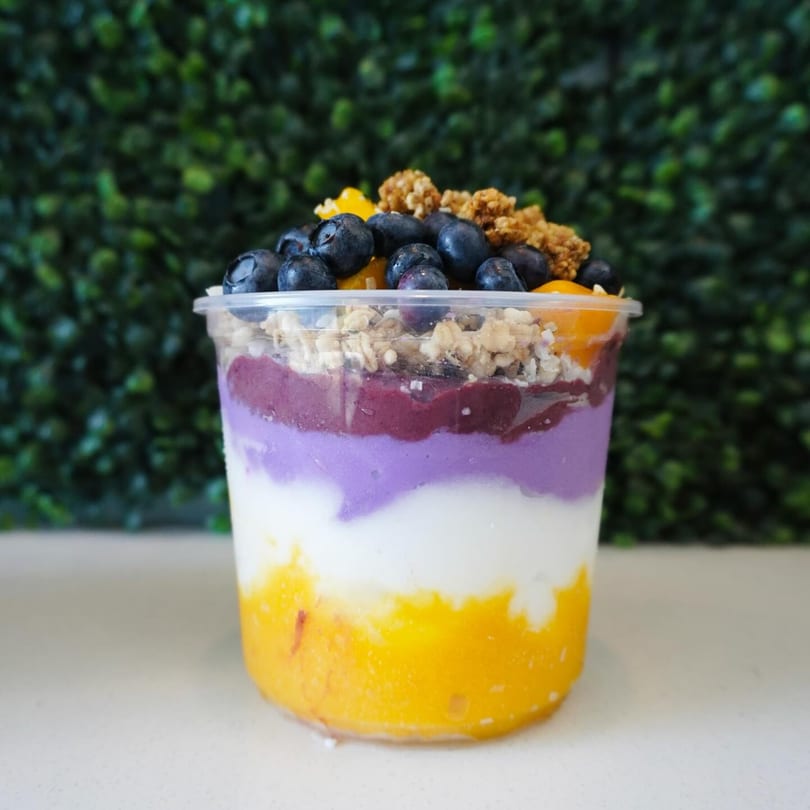 Layered smoothie bowl with yellow, white, purple, and dark purple, topped with blueberries and granola.